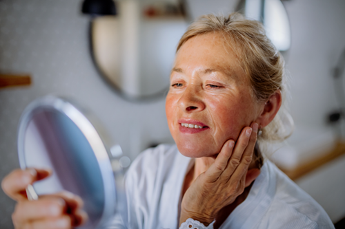 Adult woman checking her face in the mirror to see if her rosacea has cleared up